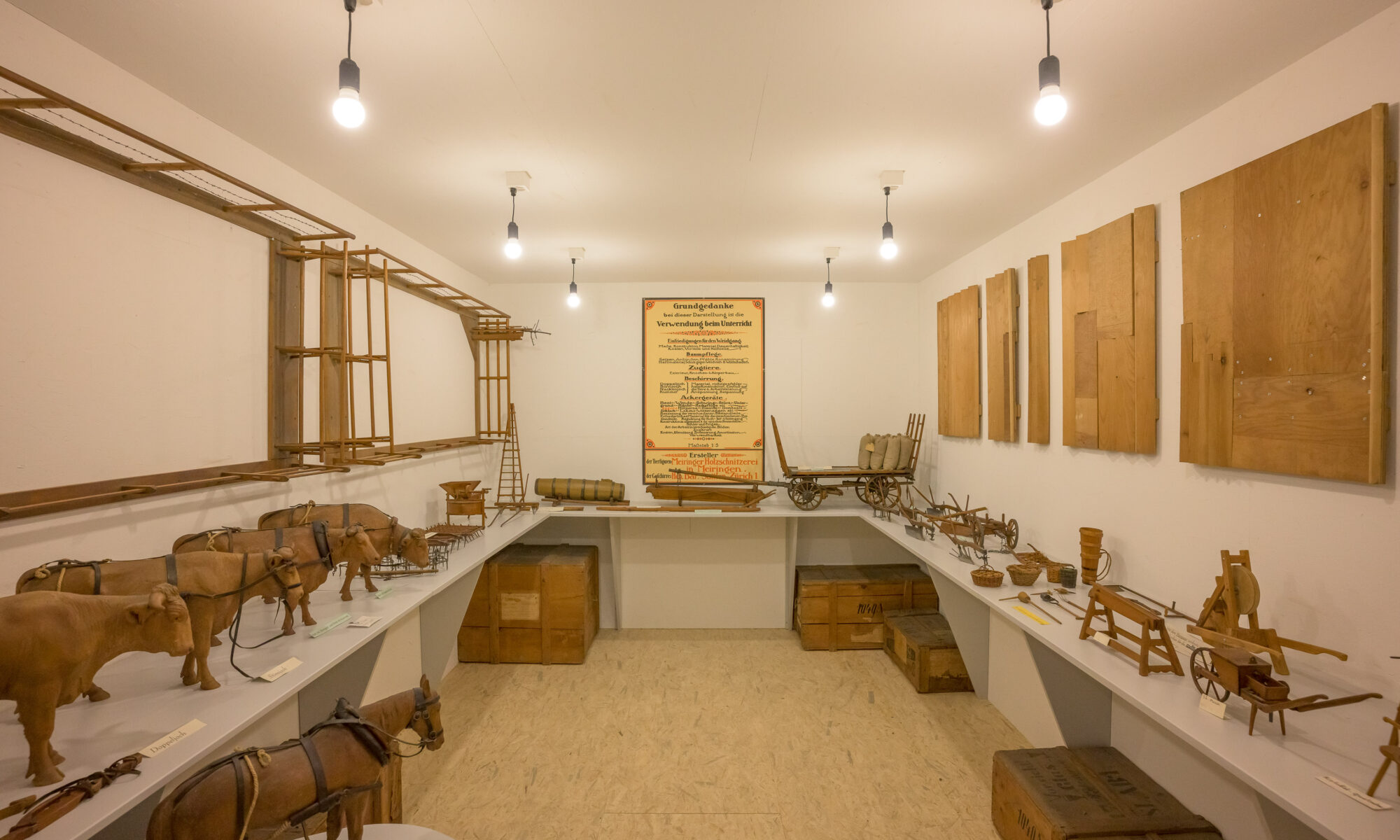 Raum mit weissen Wänden, darin diverse landwirtschaftliche Modelle aus Holz und ein Plakat an der Wand