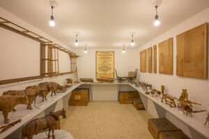 Raum mit weissen Wänden, darin diverse landwirtschaftliche Modelle aus Holz und ein Plakat an der Wand