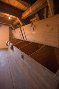 grosse, in den Raum eingebaute Holztruhen mit hochgeklappten Deckeln und Unterteilungen im Innern